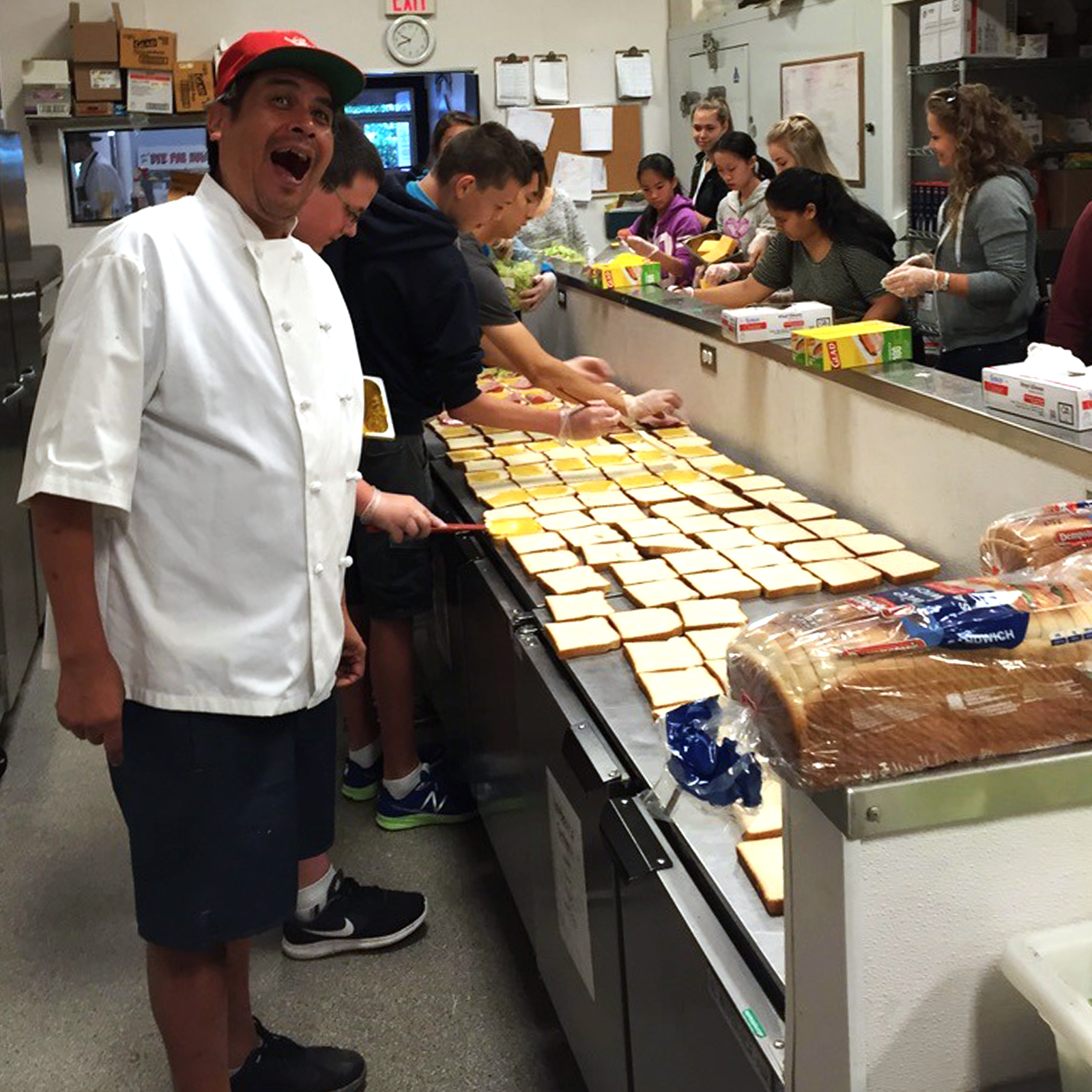 Diverse Save On Meats kitchen team prepares meal token sandwiches.